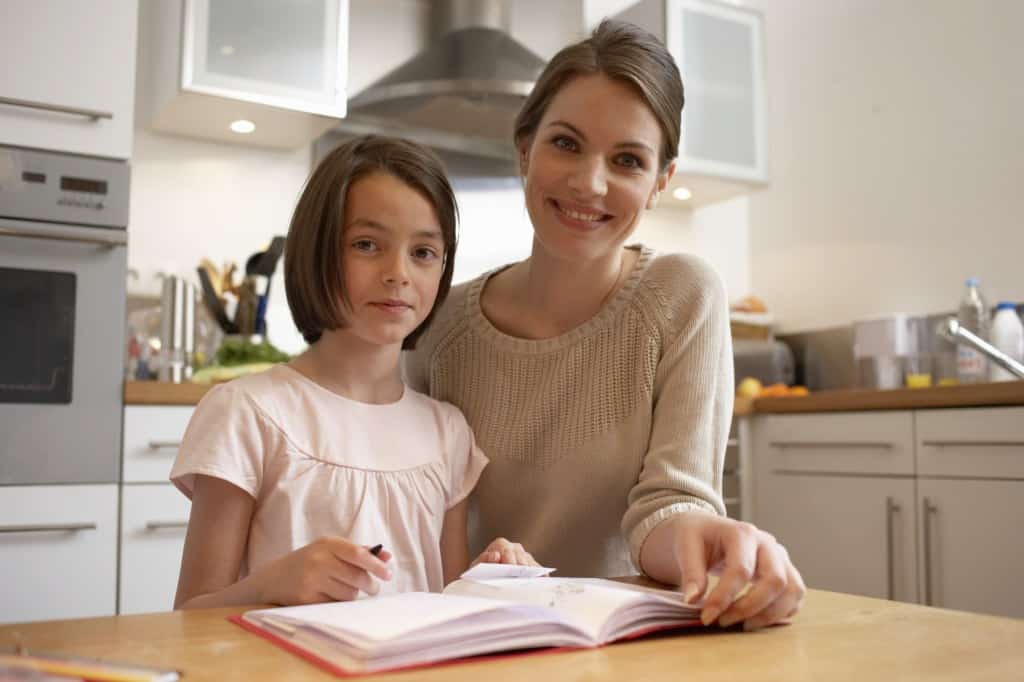 Mother and daughter (6-8) with exercise book in kitchen, portrait